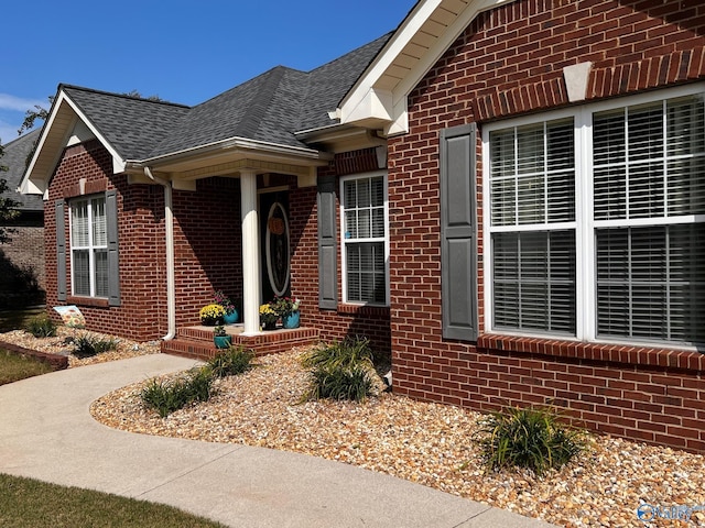 property entrance featuring roof with shingles and brick siding