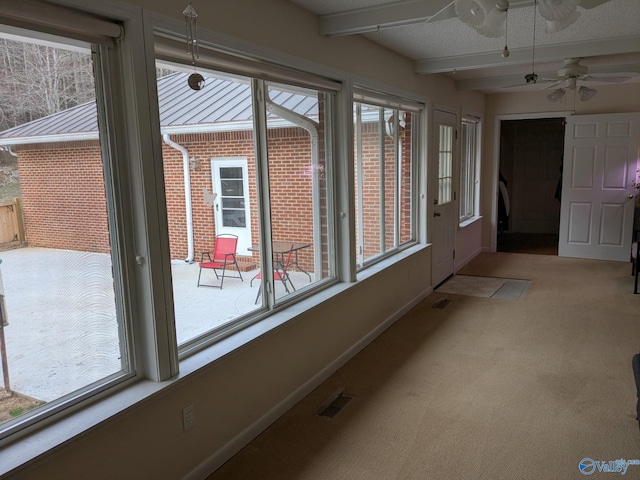 unfurnished sunroom with a ceiling fan, visible vents, and beamed ceiling