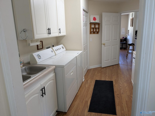 clothes washing area featuring cabinet space, baseboards, light wood-type flooring, separate washer and dryer, and a sink