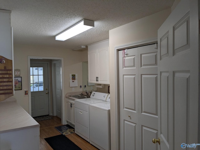 laundry area with dark wood-style floors, washing machine and clothes dryer, cabinet space, a sink, and a textured ceiling