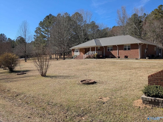 view of front of house featuring brick siding, covered porch, metal roof, and a front yard