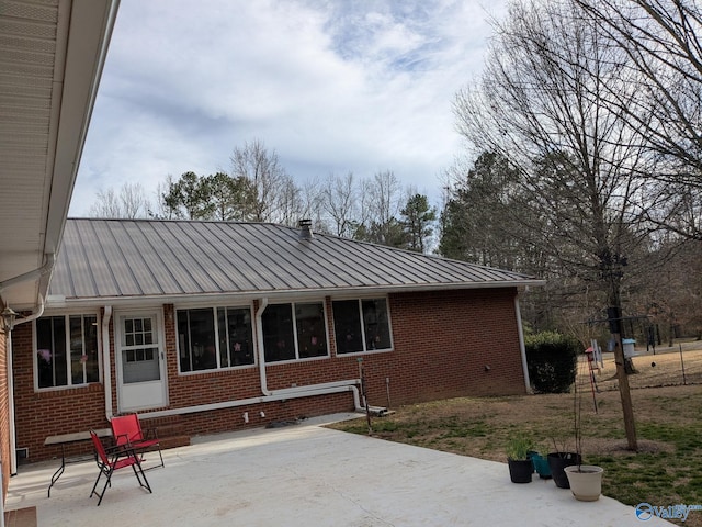 back of property featuring a patio area, a standing seam roof, metal roof, and brick siding