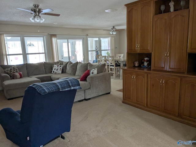 living area with ceiling fan, a textured ceiling, and light colored carpet