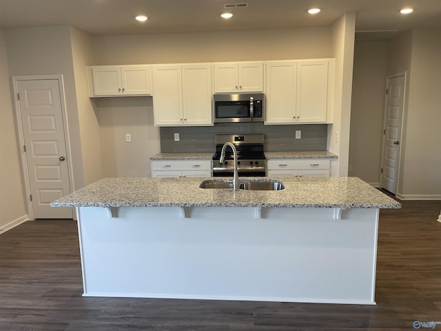 kitchen with a kitchen bar, white cabinetry, an island with sink, stainless steel appliances, and backsplash