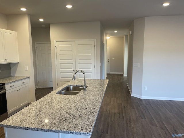 kitchen featuring white cabinetry, a kitchen island with sink, sink, and light stone counters