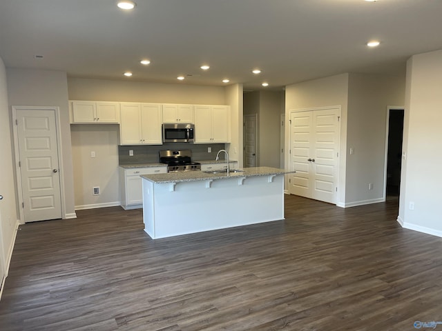 kitchen with a kitchen island with sink, light stone counters, stainless steel appliances, and white cabinets