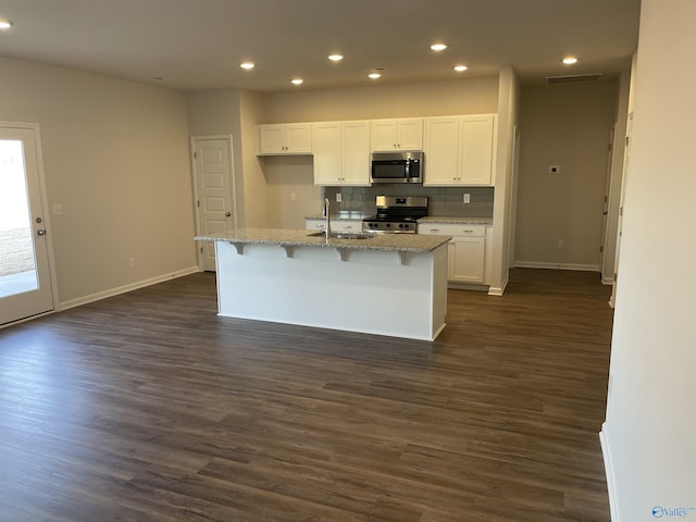 kitchen with white cabinetry, light stone counters, dark hardwood / wood-style flooring, an island with sink, and stainless steel appliances