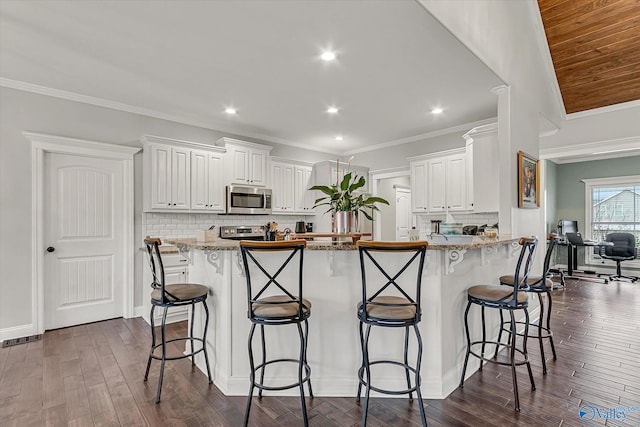 kitchen featuring light stone counters, a breakfast bar, dark wood-style floors, appliances with stainless steel finishes, and white cabinetry