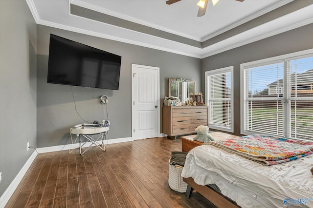 bedroom featuring ornamental molding, a tray ceiling, dark wood-type flooring, and baseboards