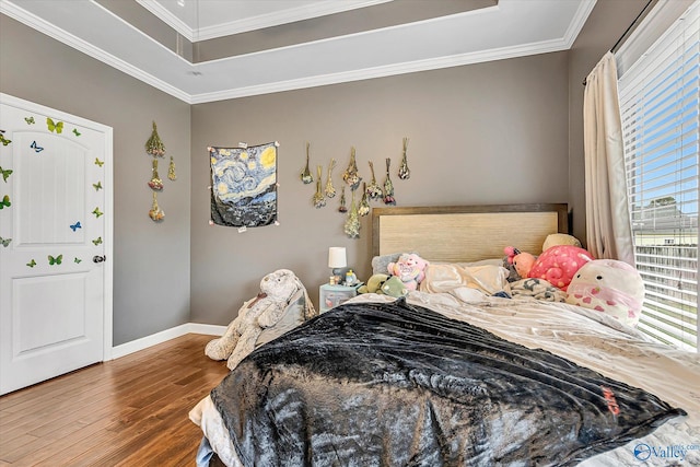 bedroom featuring a tray ceiling, crown molding, baseboards, and wood finished floors