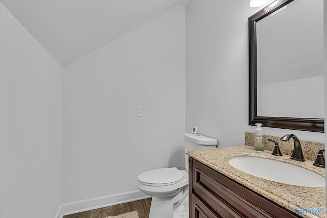 half bathroom featuring baseboards, toilet, lofted ceiling, wood finished floors, and vanity