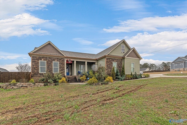 view of front of property featuring covered porch, stone siding, a front lawn, and fence