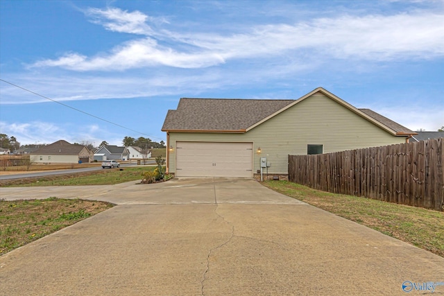 view of home's exterior featuring a garage, concrete driveway, fence, and a shingled roof