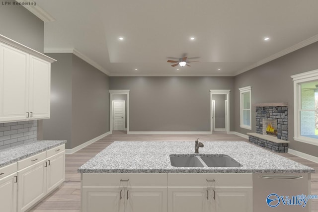 kitchen featuring a fireplace, white cabinetry, sink, and a center island with sink