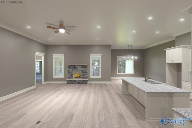 kitchen featuring white cabinets, a stone fireplace, sink, hanging light fixtures, and light wood-type flooring