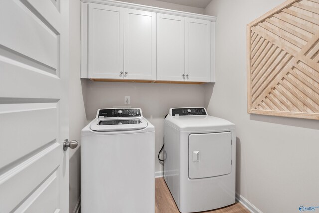 washroom featuring cabinets, washing machine and clothes dryer, and light hardwood / wood-style flooring