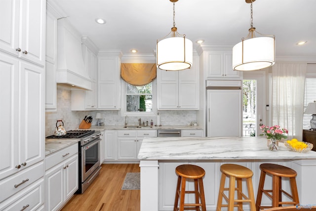 kitchen with white cabinets, a kitchen bar, high quality appliances, and premium range hood