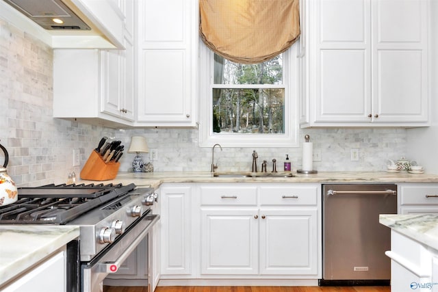 kitchen with sink, premium range hood, stainless steel appliances, light stone counters, and white cabinets