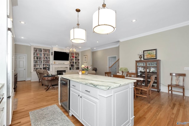 kitchen featuring light wood-type flooring, a kitchen island, pendant lighting, beverage cooler, and white cabinets