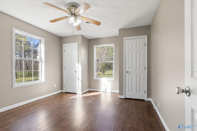 unfurnished bedroom featuring ceiling fan, dark hardwood / wood-style floors, a textured ceiling, and multiple windows