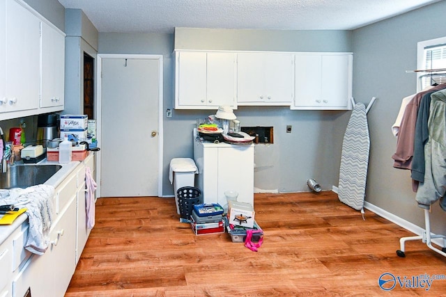 kitchen featuring white cabinetry, sink, light hardwood / wood-style flooring, and a textured ceiling