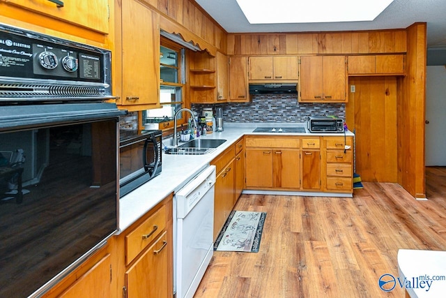 kitchen featuring black appliances, tasteful backsplash, sink, a skylight, and light hardwood / wood-style flooring