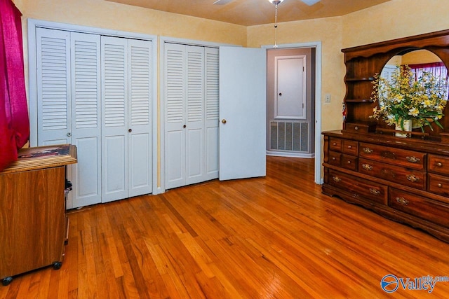 bedroom with hardwood / wood-style floors, ceiling fan, and two closets