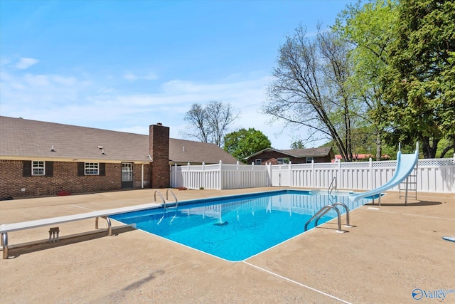 view of pool featuring a fenced in pool, a water slide, fence, a diving board, and a patio