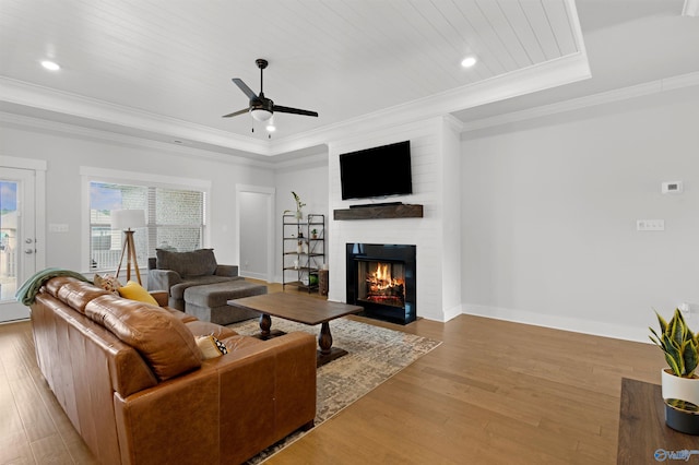 living room with light hardwood / wood-style flooring, a tray ceiling, a fireplace, and ornamental molding