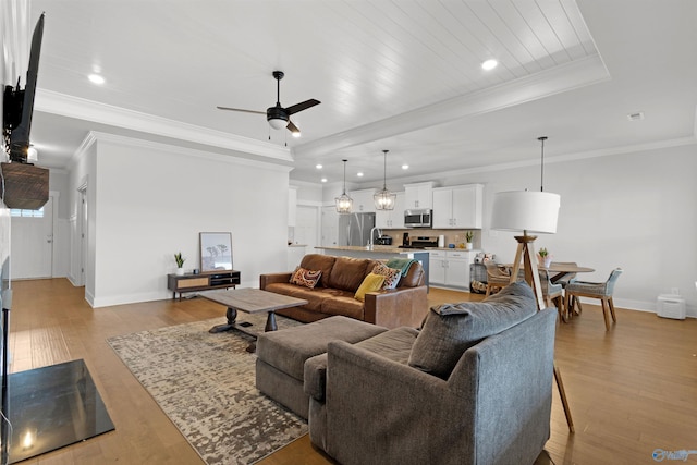 living room with crown molding, ceiling fan, a raised ceiling, and light hardwood / wood-style flooring