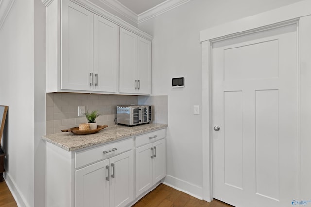 kitchen featuring backsplash, ornamental molding, hardwood / wood-style floors, and white cabinets