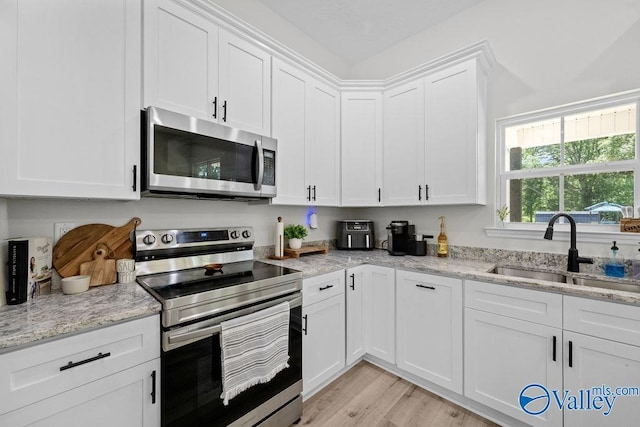 kitchen featuring sink, white cabinetry, light stone counters, stainless steel appliances, and light hardwood / wood-style floors