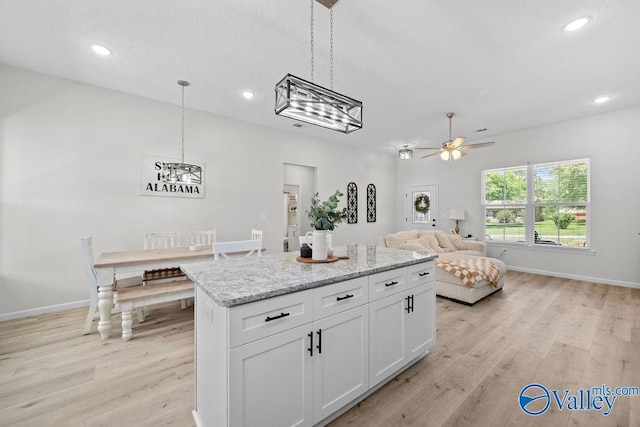 kitchen with white cabinetry, light stone countertops, light hardwood / wood-style floors, a kitchen island, and decorative light fixtures