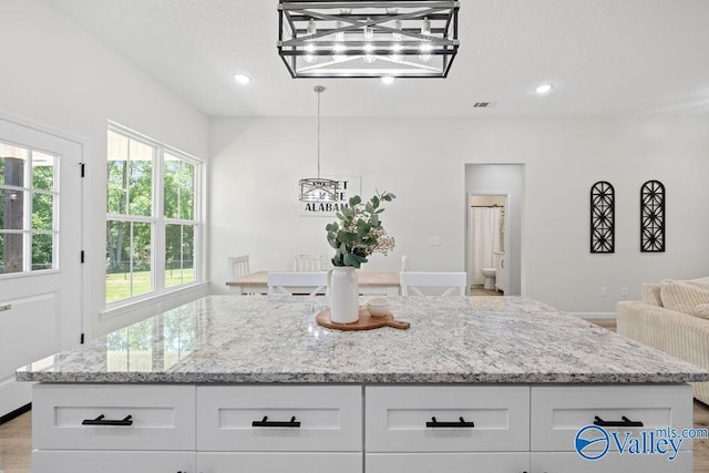 kitchen featuring light stone countertops, light wood-type flooring, hanging light fixtures, and white cabinets