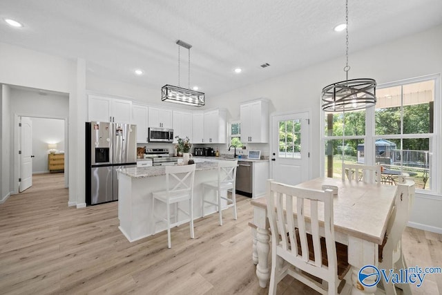 kitchen with light hardwood / wood-style flooring, appliances with stainless steel finishes, hanging light fixtures, white cabinets, and a kitchen island