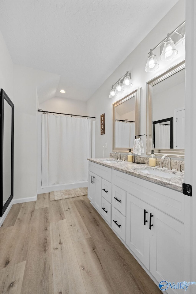 bathroom with vaulted ceiling, hardwood / wood-style floors, vanity, walk in shower, and a textured ceiling