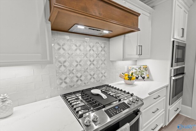 kitchen featuring white cabinets, decorative backsplash, light stone counters, custom range hood, and appliances with stainless steel finishes