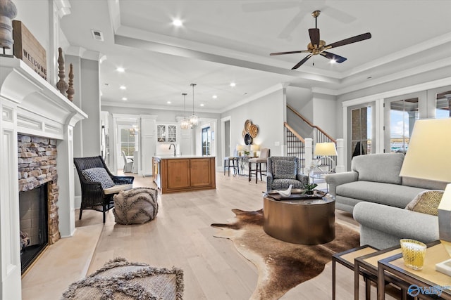 living room featuring a stone fireplace, ceiling fan with notable chandelier, light hardwood / wood-style flooring, and plenty of natural light