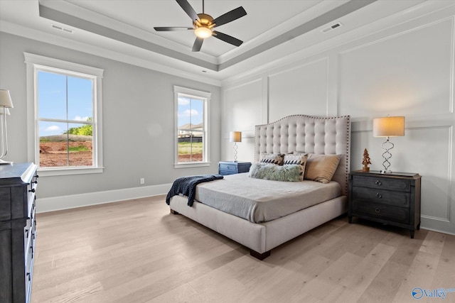 bedroom featuring light hardwood / wood-style floors, multiple windows, and a tray ceiling