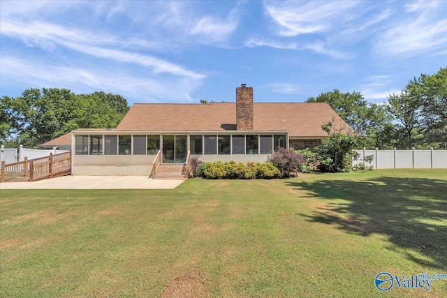 back of property with a sunroom, a patio area, and a lawn