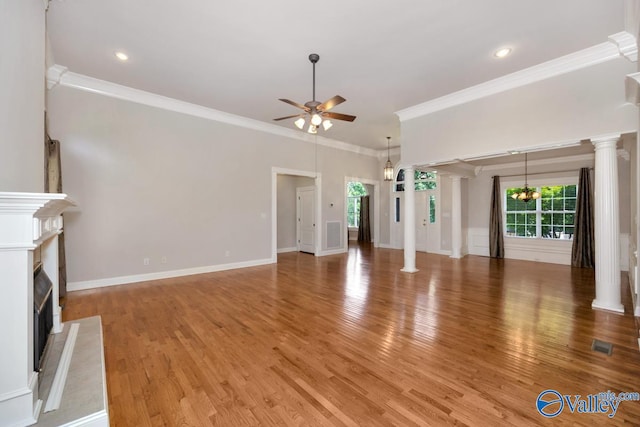 unfurnished living room with decorative columns, crown molding, light wood-type flooring, ceiling fan with notable chandelier, and a towering ceiling