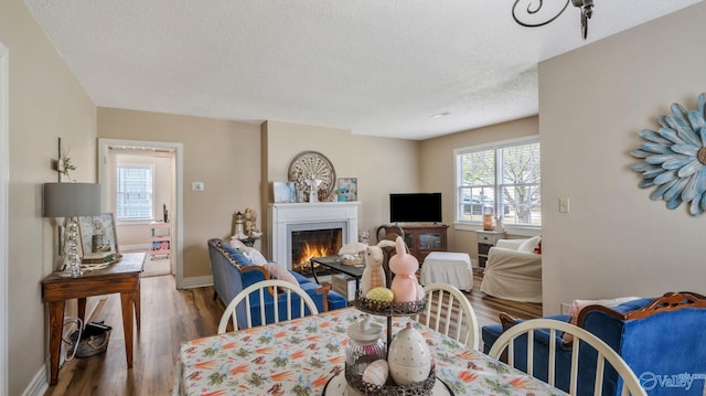 dining room featuring a warm lit fireplace, wood finished floors, a textured ceiling, and baseboards