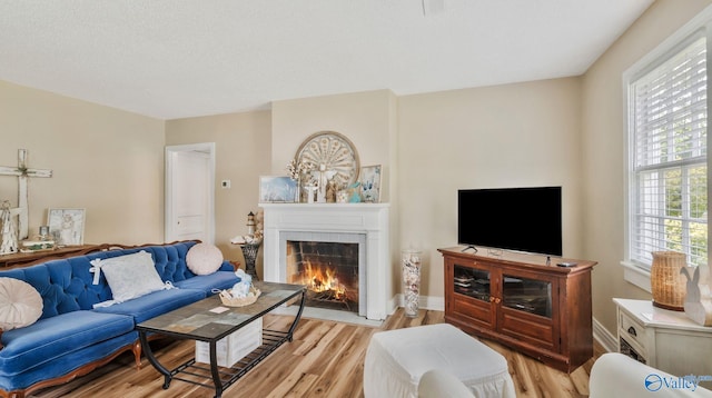 living room with a tiled fireplace, baseboards, and light wood-style flooring