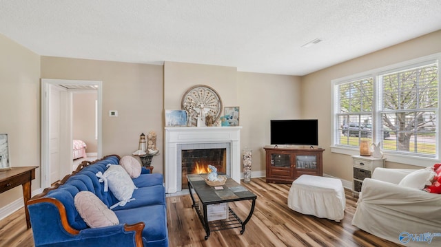 living area featuring baseboards, a tile fireplace, wood finished floors, and a textured ceiling