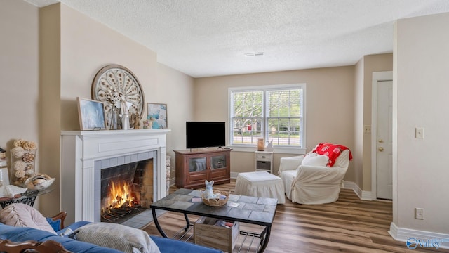 living area featuring wood finished floors, a textured ceiling, a tile fireplace, baseboards, and visible vents