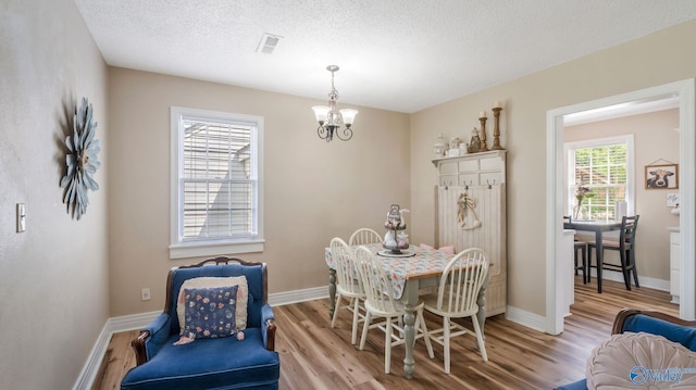dining room with visible vents, light wood-type flooring, baseboards, a textured ceiling, and a notable chandelier