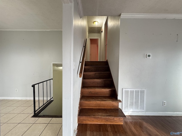 stairway with crown molding, tile patterned flooring, and a textured ceiling