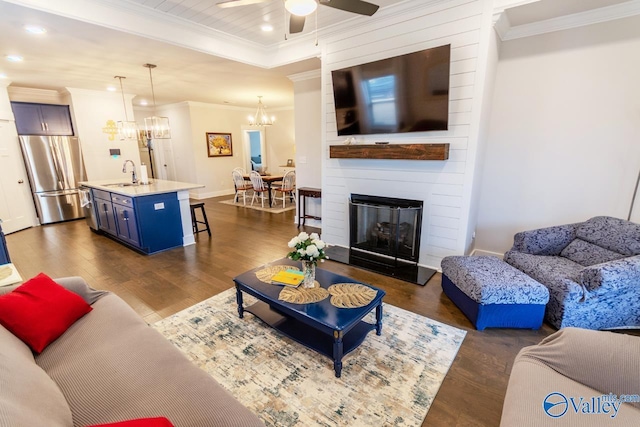 living room featuring dark hardwood / wood-style flooring, ceiling fan with notable chandelier, crown molding, sink, and a fireplace