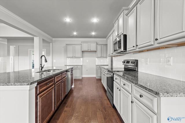 kitchen with sink, appliances with stainless steel finishes, dark stone countertops, ornamental molding, and dark wood-type flooring