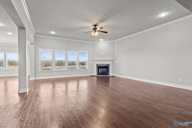 unfurnished living room featuring dark wood-type flooring, ceiling fan, crown molding, and a stone fireplace